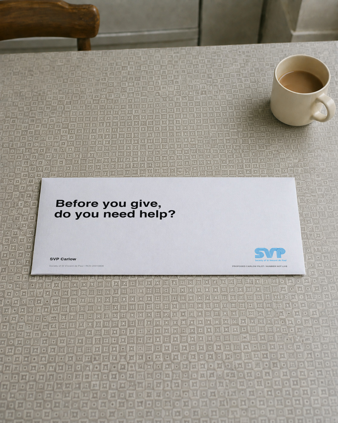 An SVP envelope on a kitchen table beside a cup of tea asks “Before you give, do you need help?” The envelope carries the official logo and proposed-pilot status.