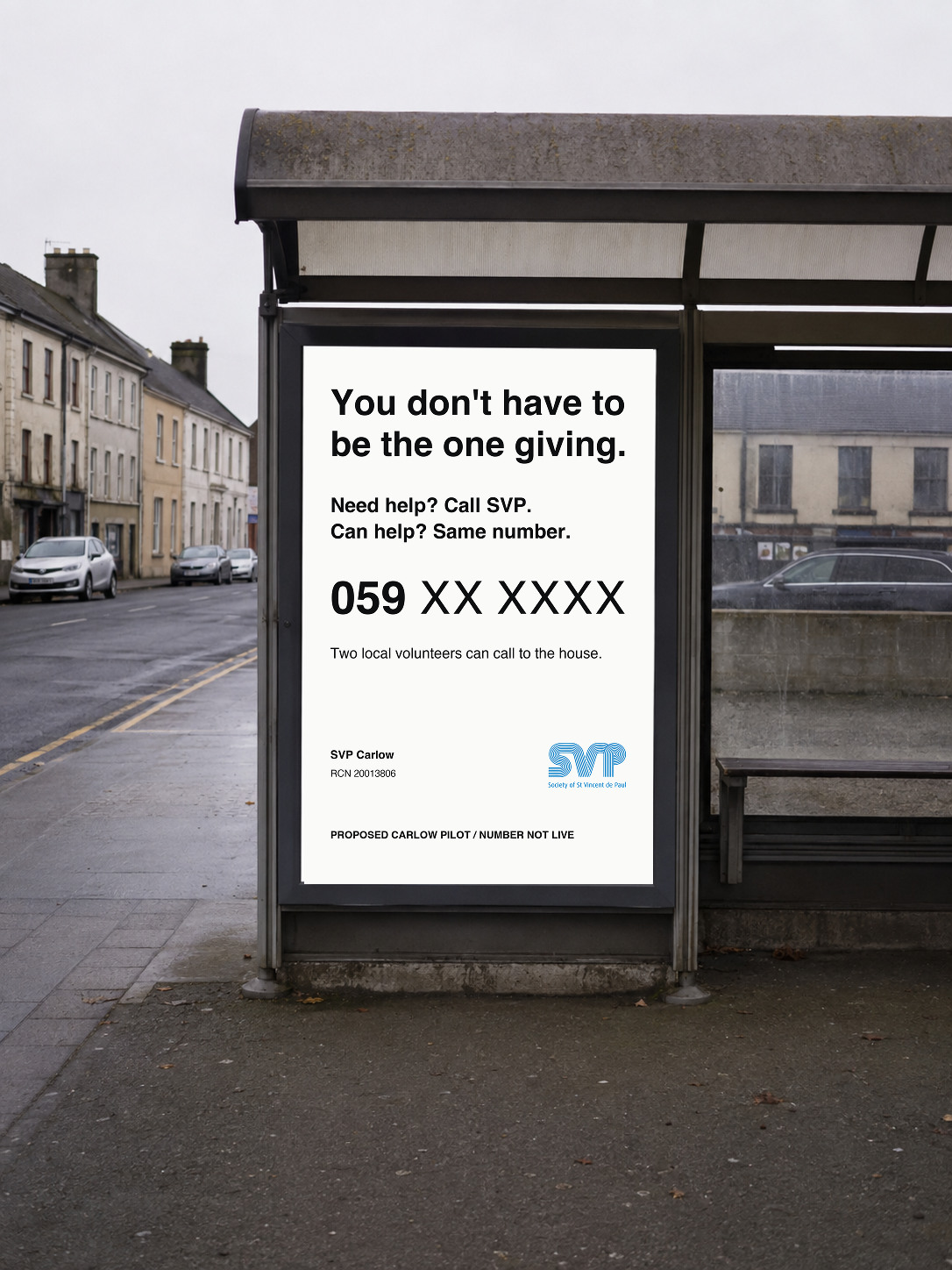 A bus-shelter poster reads “You don’t have to be the one giving”, followed by both call invitations, 059 XX XXXX and “Two local volunteers can call to the house.” The concept is labelled as a proposed Carlow pilot; the number is not live.